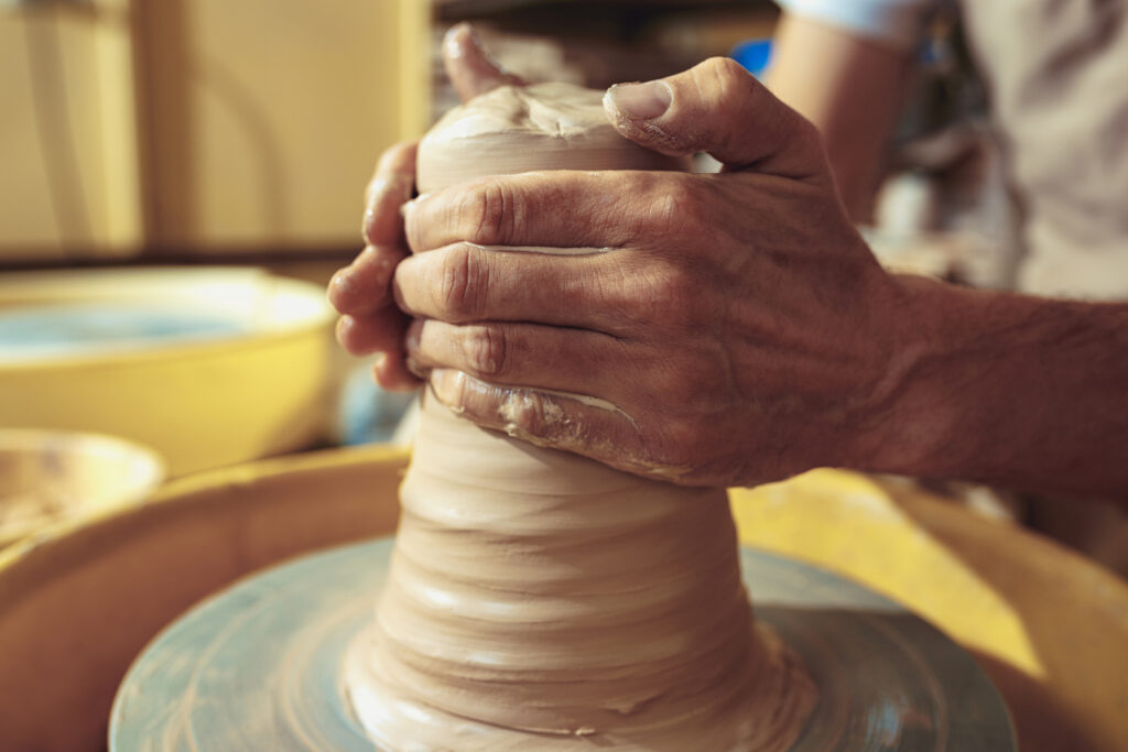 Creating a jar or vase of white clay close-up. Master crock. Man hands making clay jug macro. The sculptor in the workshop makes a jug out of earthenware closeup. Twisted potter's wheel.